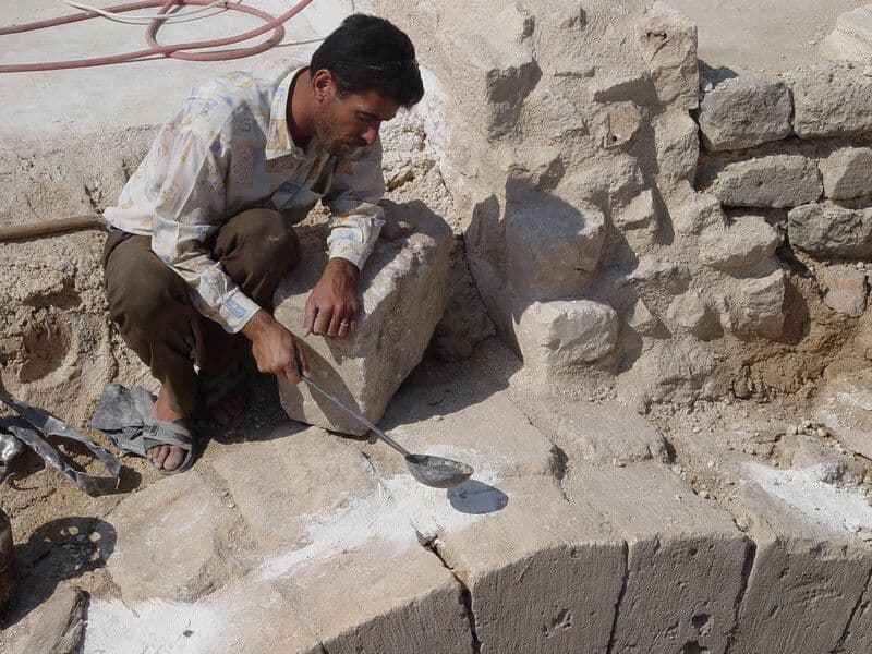 A man ladles a substance onto a stone arch at the Citadel of Aleppo.
