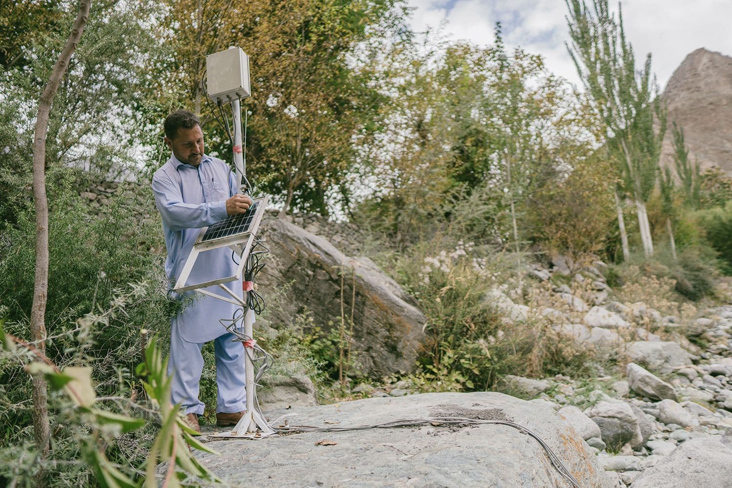 A man stands amid small trees checking a flood warning system.