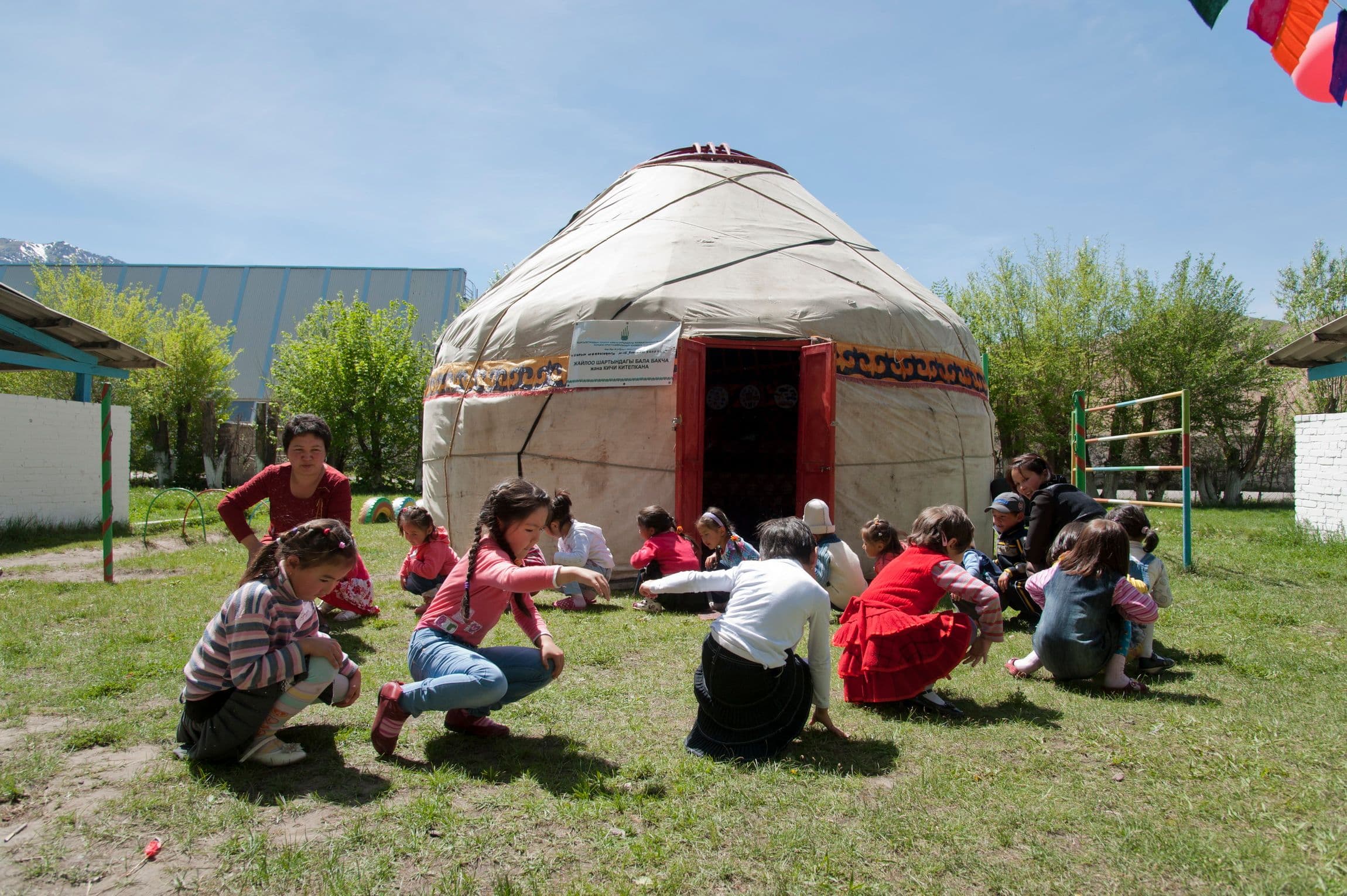 Children play in a circle outside a yurt classroom.