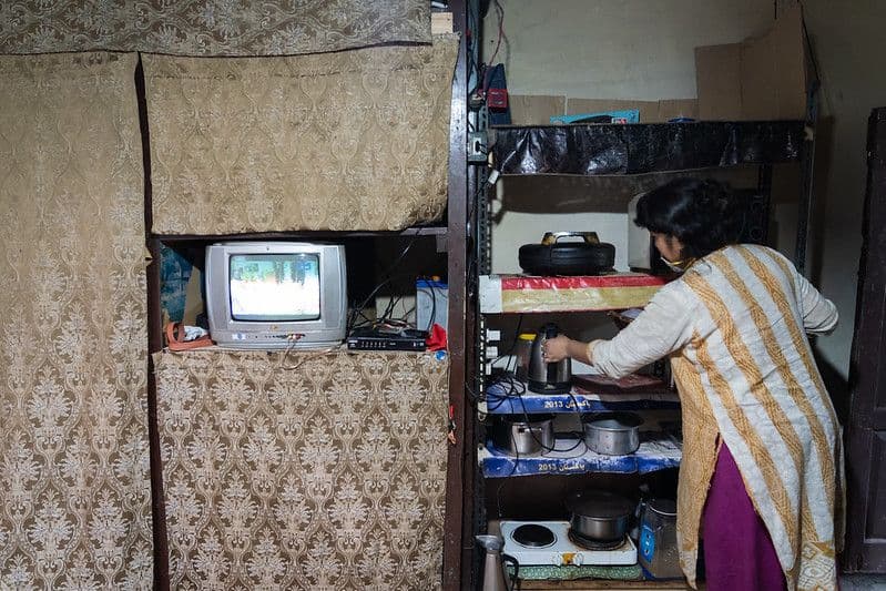 A woman uses a kettle on a shelf in her home.